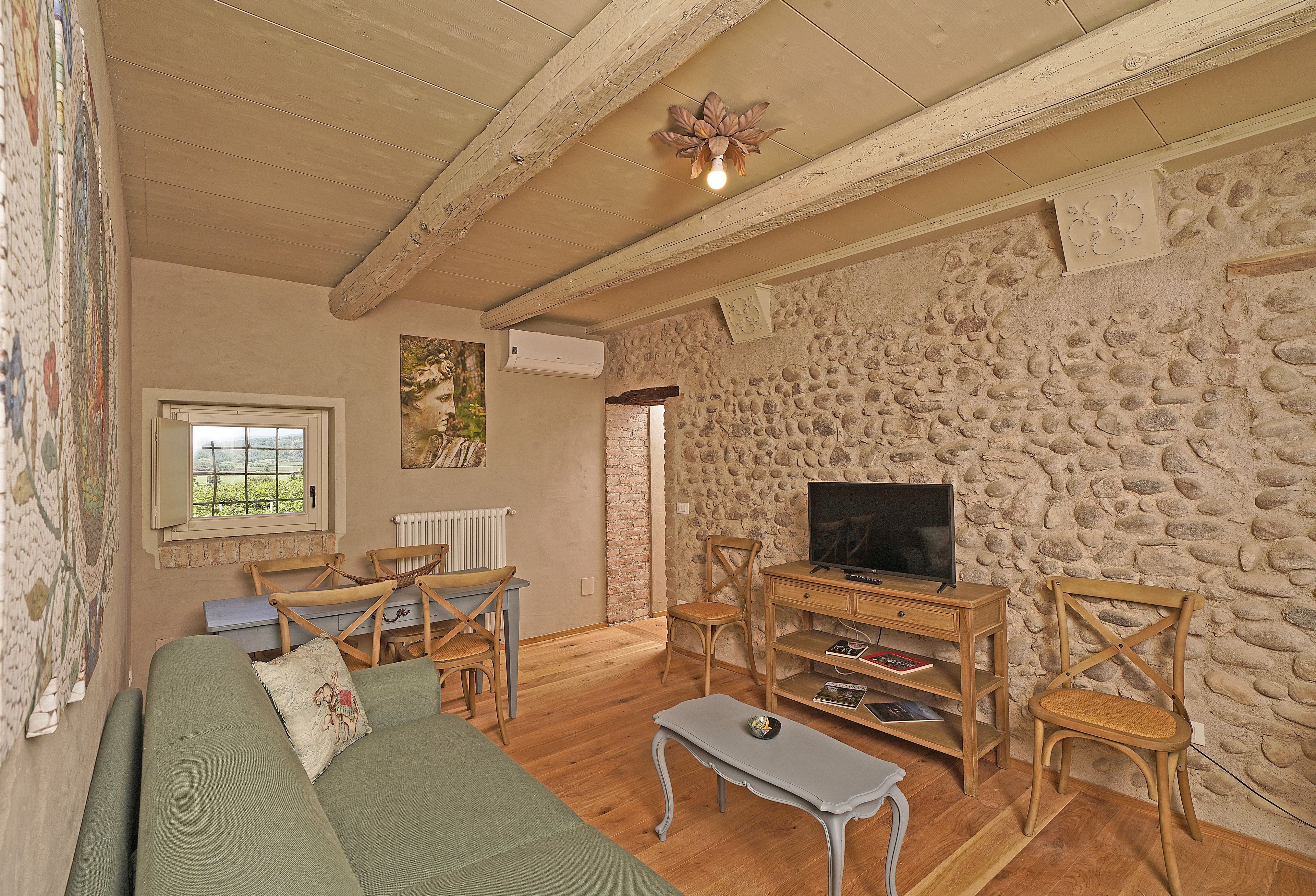 A cozy living room with a stone wall, wooden furniture, a green sofa, and a television.