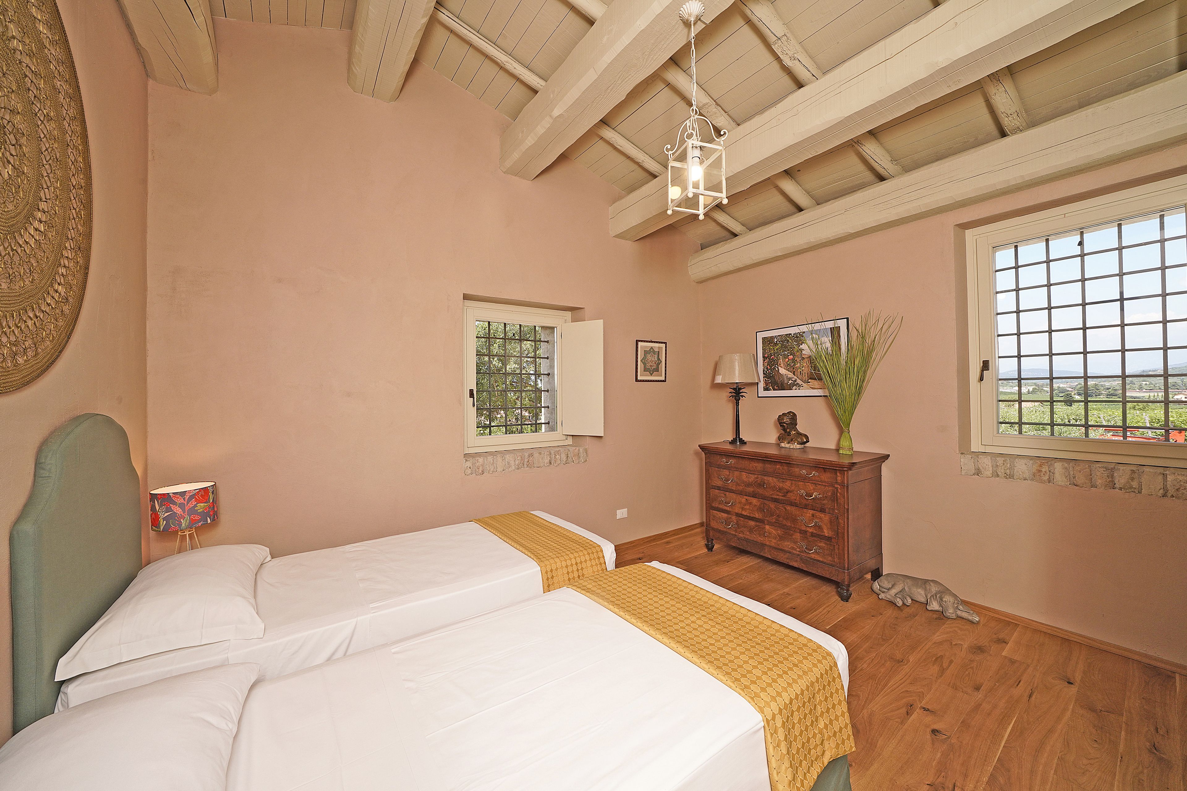 A bedroom with two beds, a dresser, a window with a view, and a ceiling with exposed beams.