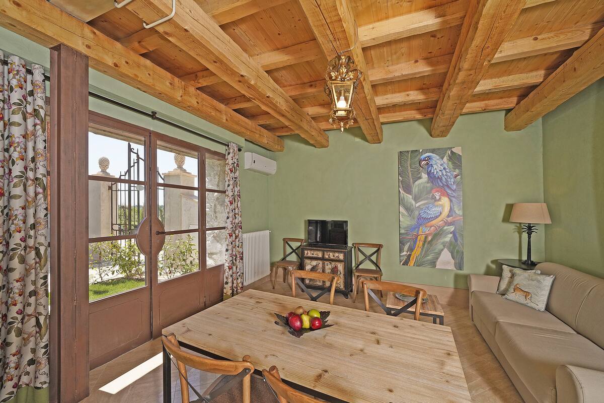 A dining area with a wooden table, chairs, a fruit bowl, a television, and a sofa.