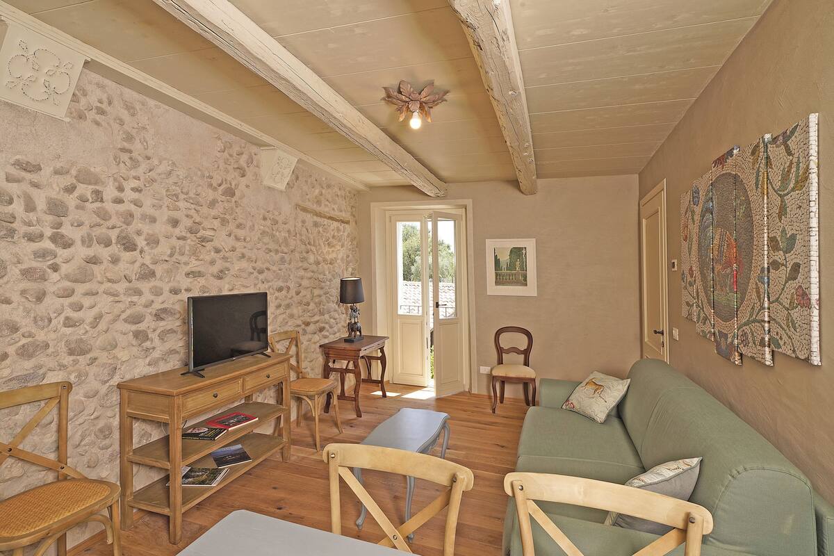 A cozy living room with a stone wall, wooden furniture, a television, and a green sofa.