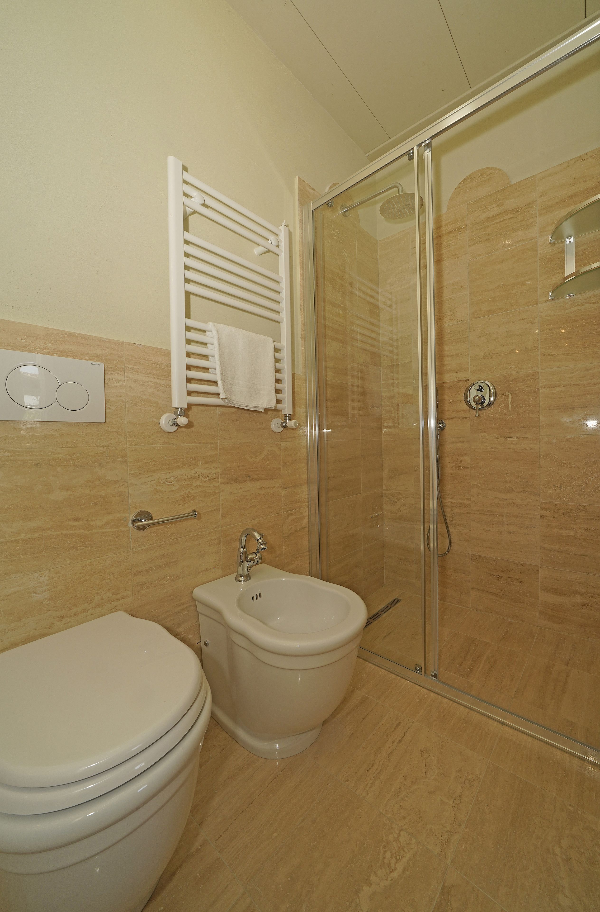 Baño con inodoro, bidé y ducha con mampara de vidrio.