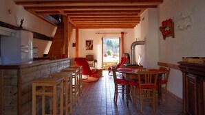 Une cuisine rustique avec des poutres en bois, un coin repas avec des chaises rouges et une vue sur l’extérieur.