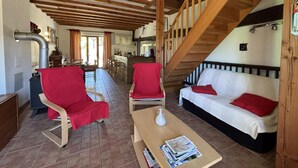 Une pièce chaleureuse avec un plafond en bois, un canapé, deux fauteuils, une table avec des magazines et un escalier.