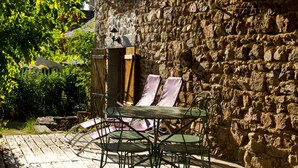Une terrasse en bois avec un mur en pierre, des chaises en métal et une table.