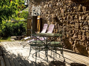 Een houten terras met een stenen muur, metalen stoelen en een tafel.