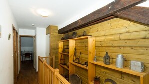 Un intérieur en bois avec un escalier, des étagères en bois contenant divers outils et récipients, et un coin repas visible au fond.