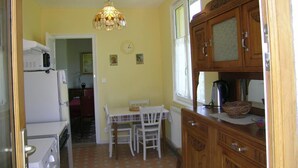 Une cuisine compacte comprenant une table à manger, des chaises, un réfrigérateur, un lave-linge, des placards en bois et un luminaire suspendu.