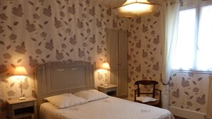 Une chambre à coucher avec un lit, deux tables de chevet avec des lampes, une chaise et une fenêtre avec des rideaux.