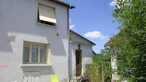 Un bâtiment à deux étages, à l’extérieur blanc, avec une porte d’entrée, un petit porche doté d’une chaise et un escalier menant à l’entrée.