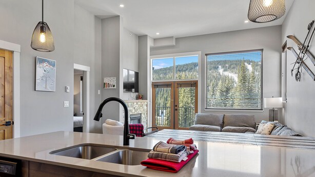 Una cocina moderna con una isla grande, lavavajillas integrado y vistas a un dormitorio con sofá y ventana con vista al bosque.