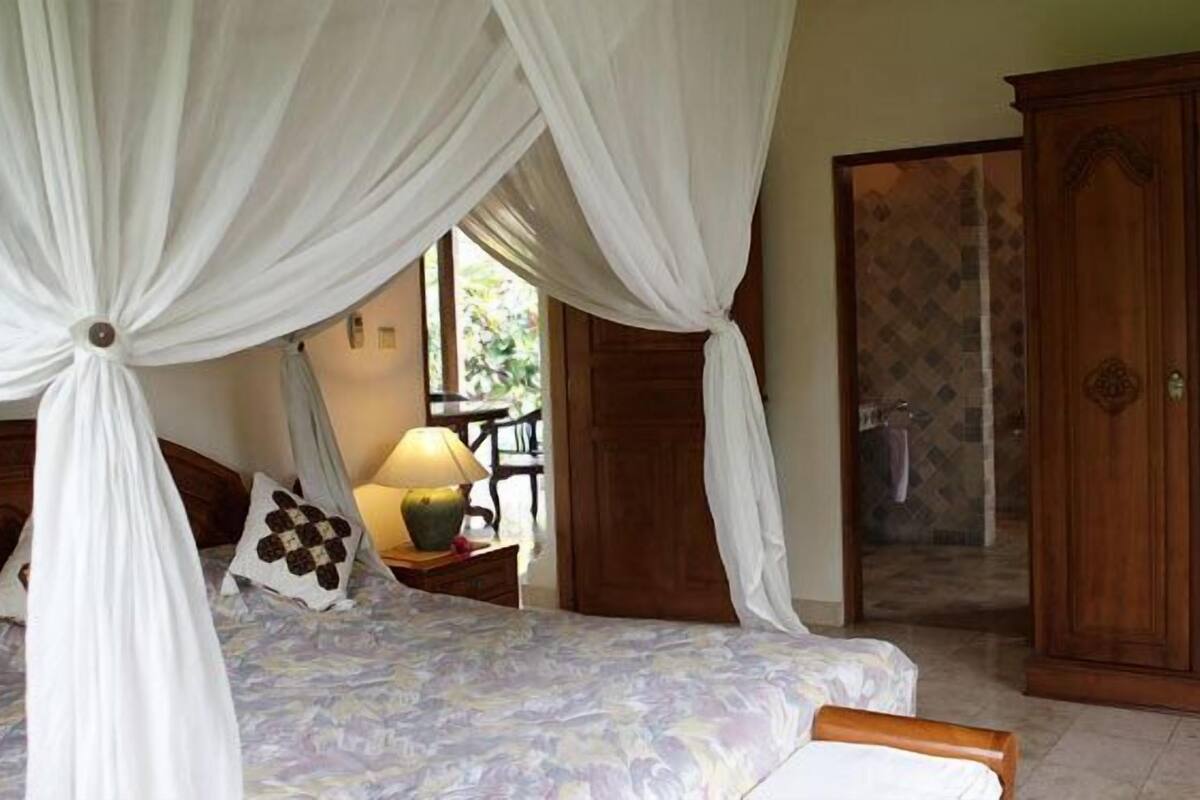 A bedroom with a bed, a nightstand, a lamp, a wardrobe, and a window with curtains.