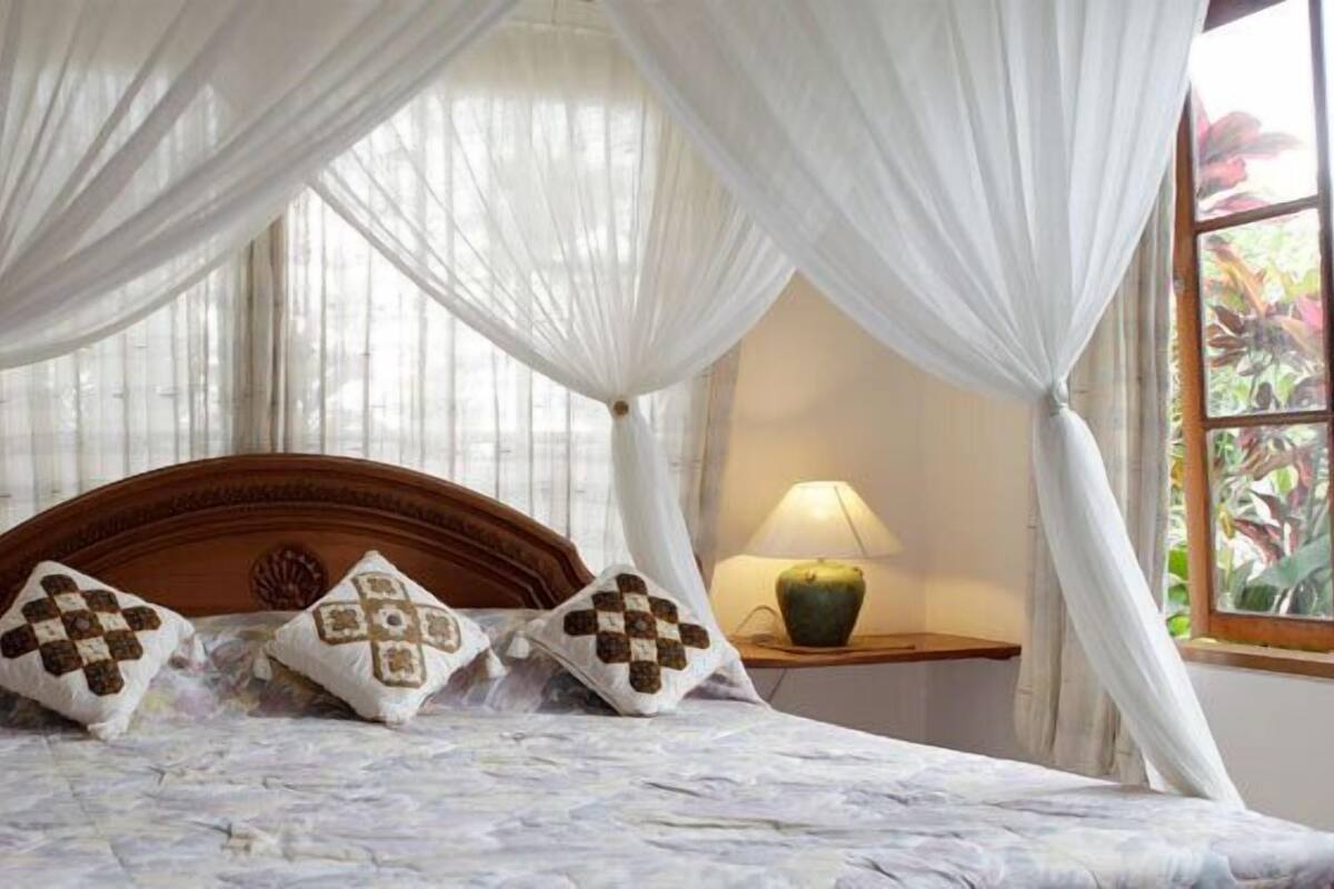A bed with a canopy, two bedside lamps, and a window with curtains.