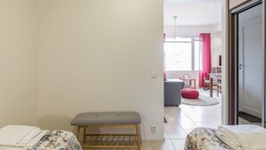 Een hotelkamer met een bed, een bankje, een tafeltje en uitzicht op de aangrenzende eetruimte.
