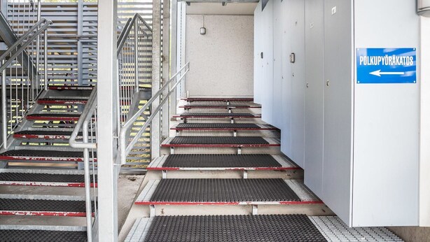 Een set metalen trappen met rode en zwarte treden die naar een deur leiden, waarop 'POLKUPYORAKATOS' staat.
