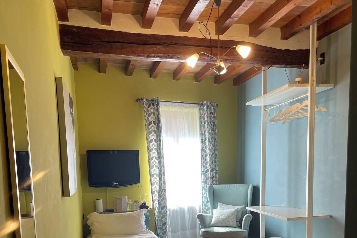 A bedroom with two beds, a chair, a TV, and a window with curtains.