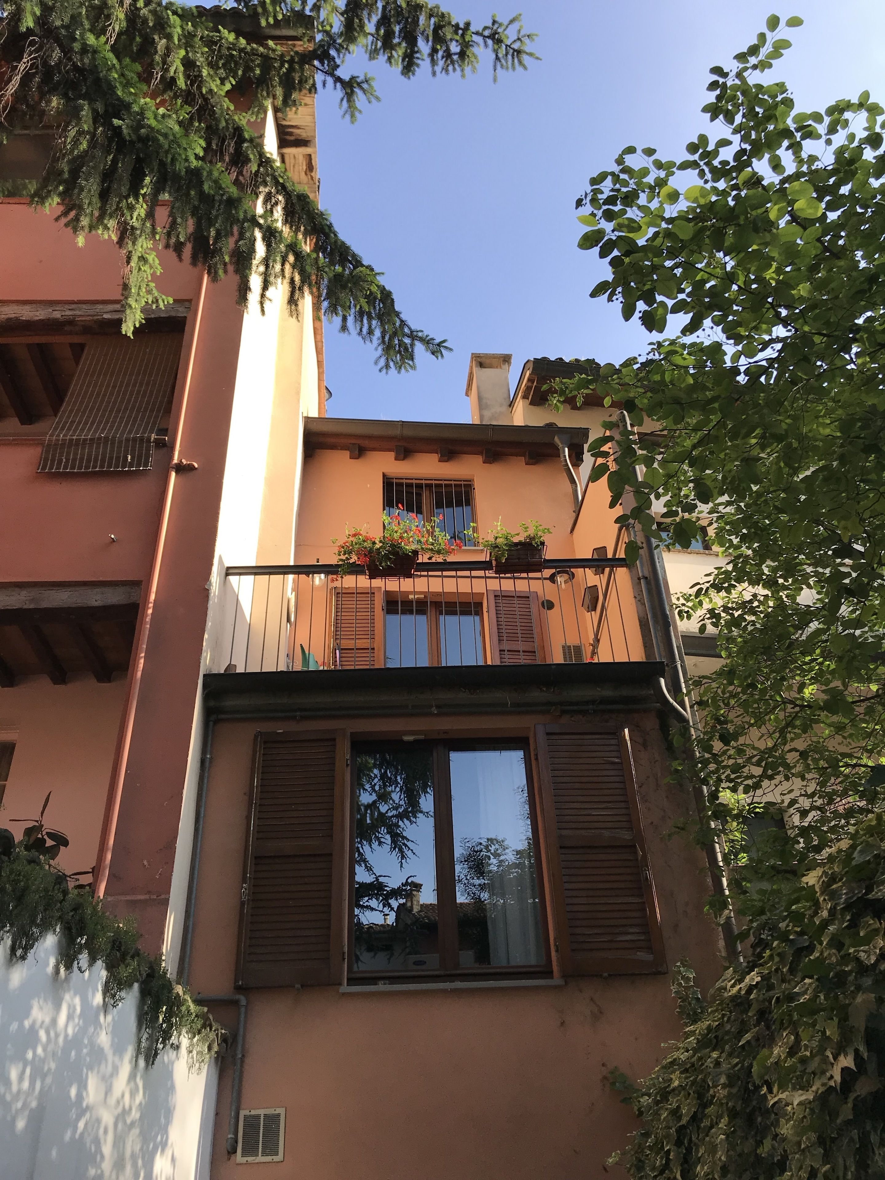 A two-story building with a balcony, a window with shutters, and a small door.
