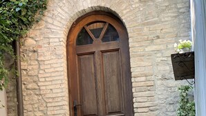 A rustic stone building with a wooden door, potted plants, and a small table with a chair. - Le camere di Bsuites (Parma)
