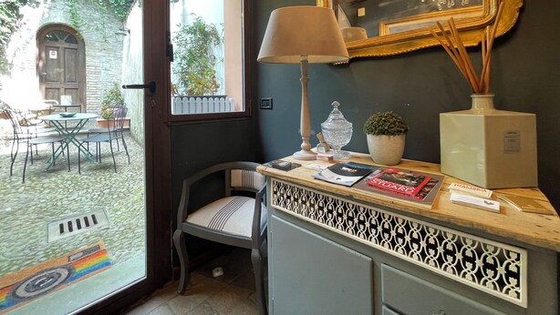 A room with a window, a table with chairs, a lamp, a mirror, and a cabinet with decorative items. - Le camere di Bsuites (Parma)