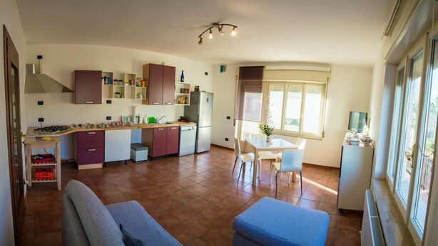 A compact kitchen with a dining area, a sofa, and a window with blinds. - B&B Marameo (Udine)