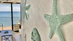Ein Zimmer mit einer großen Meersterndeko an der Wand, Blick auf das Meer durch ein Fenster und ein Stuhl und ein Tisch im Vordergrund.