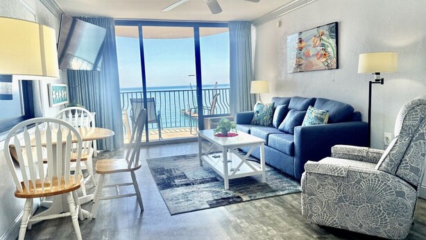 Ein Wohnzimmer mit Sofa, Sesseln, einem Couchtisch, einem Deckenventilator und Blick auf den Ozean.