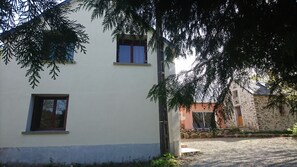 A two-story building with a white facade, a small window, and a door. There is a stone building in the background with a sloped roof. - GITE WITH SWIMMING POOL, ping pong, 45 min le mans, located alpes mancelles (MONT SAINT JEAN)