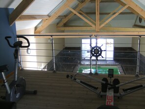 A gym with exercise equipment, a wooden beam ceiling, and a window. - GITE WITH SWIMMING POOL, ping pong, 45 min le mans, located alpes mancelles (MONT SAINT JEAN)