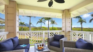 A covered outdoor seating area with wicker furniture and a glass table, overlooking a scenic landscape with palm trees and mountains. - Pili Mai 3L Newly Upgraded 3 Bedroom Suite in Poipu - AC, Pool & Fitness Center (Koloa)