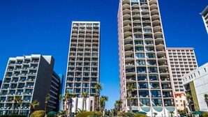A high-rise hotel with multiple balconies, a modern architectural design, and a well-maintained outdoor area with greenery. - Beautiful End Unit Oceanfront in the heart of Myrtle Beach indoor and outdoor pools 203 (Myrtle Beach)