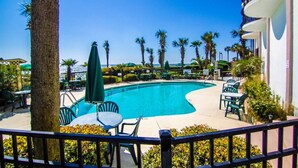 A swimming pool with lounge chairs and umbrellas, surrounded by palm trees and a clear sky. - Beautiful End Unit Oceanfront in the heart of Myrtle Beach indoor and outdoor pools 203 (Myrtle Beach)