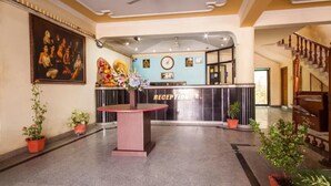 A reception area with a reception desk, a clock, and a painting on the wall. - Hotel Saurab (Dehradun)