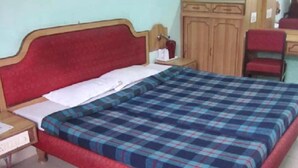 A bedroom with a bed, a nightstand, a desk, and a wardrobe. - Hotel Saurab (Dehradun)