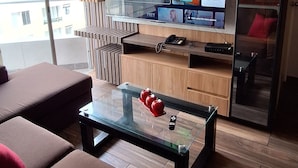 A modern living room with a large flat-screen TV mounted on a wooden wall, a glass coffee table with red decorative items, and brown sofas with red cushions. - LIMA FLAT 2 1D BETWEEN AIRPORT AND MIRAFLORES (San Miguel)