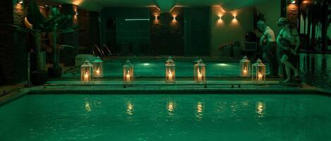A pool area with a series of lanterns along the edge, a stone wall, and a person standing by the pool.