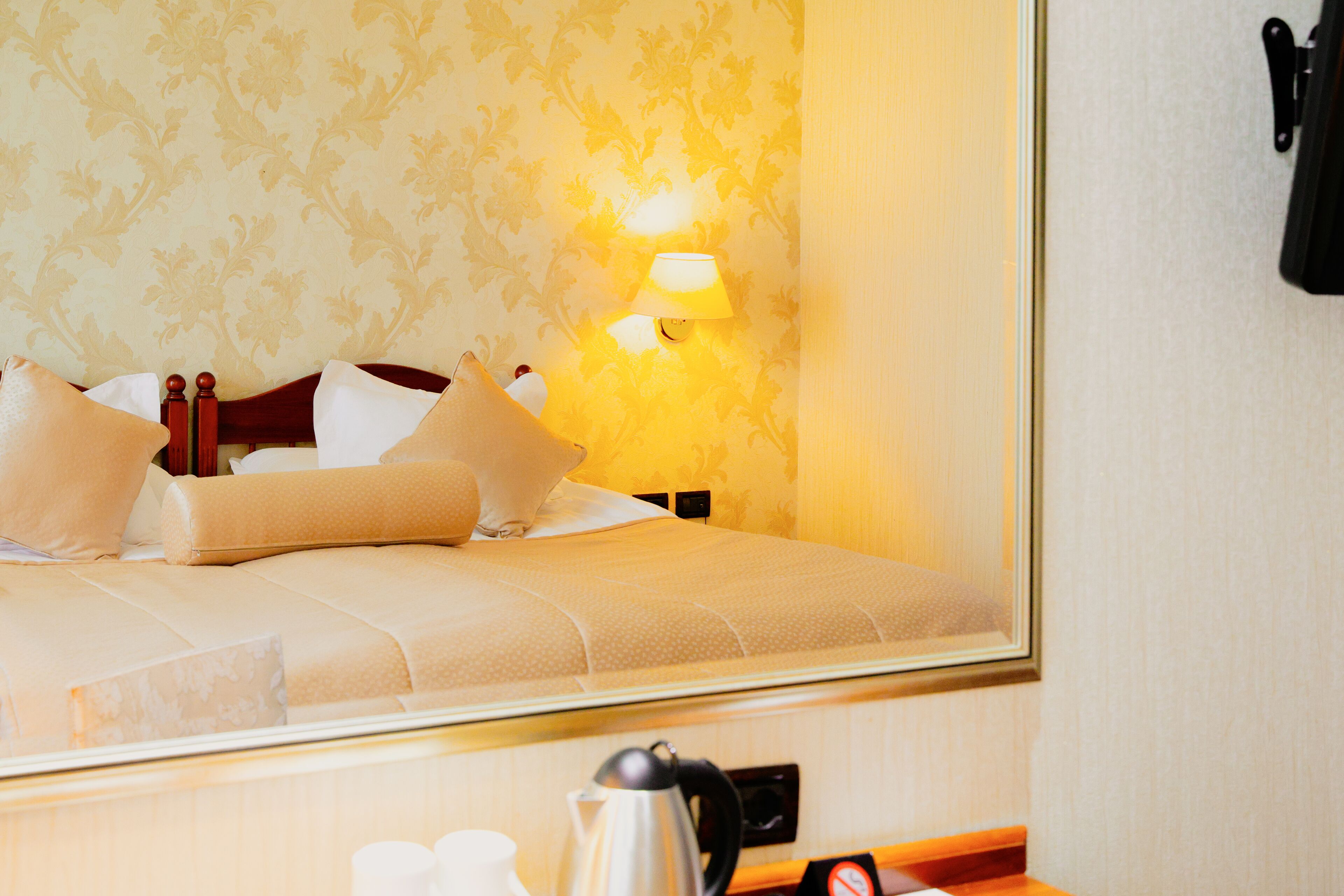 A hotel room with a bed, pillows, a nightstand, a lamp, a coffee maker, and a telephone.