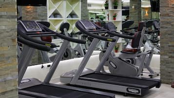 A gym with treadmills and exercise equipment, a TV mounted on the wall, and a person working out in the background.