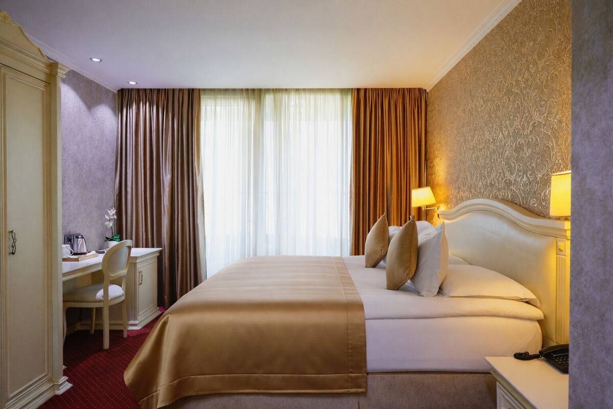 A hotel room with a large bed, a desk with a chair, a telephone, and a lamp.