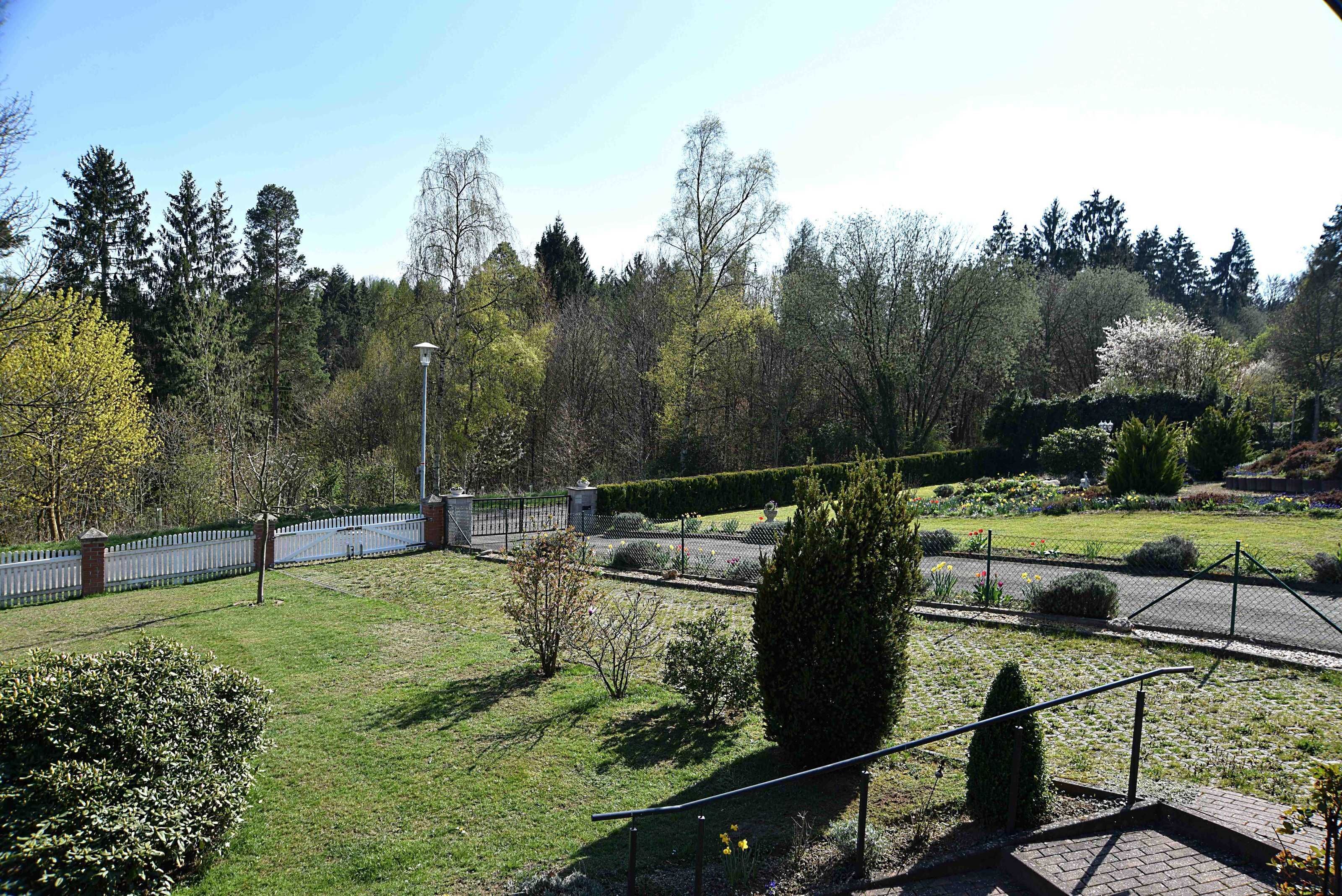 A landscaped garden with pathways, a white fence, and various trees.