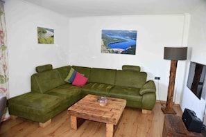 A living room with a green sofa, a wooden coffee table, and two framed pictures on the wall.