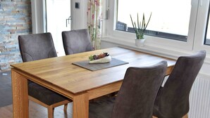 A wooden dining table with four chairs, a small plant on the table, and a window with curtains in the background. - Holiday house Karin Tassius - Holiday Karin Tassius (Vöhl)