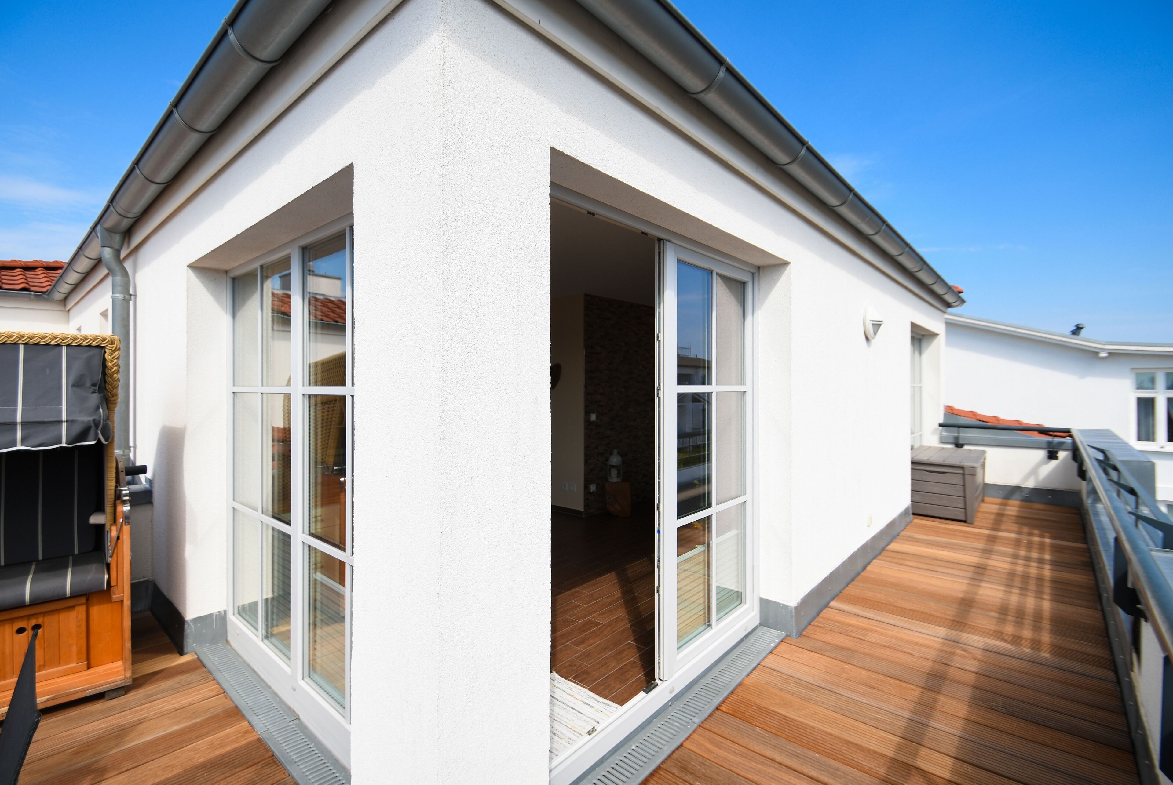 Una casa moderna con terraza de madera, grandes puertas corredizas de vidrio y un pequeño espacio de estar al aire libre.