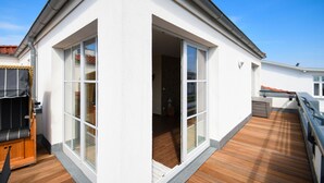 A modern house with a wooden deck, large sliding glass doors, and a small outdoor seating area. - Penthouse sea view - Apartment sea view in the penthouse (Göhren)