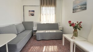 A compact room with a sofa, a small table, a bedside table, and a window with curtains. - Themis 40 steps from beach - Dionisiou Halkidiki (Paralia Dionisiou)