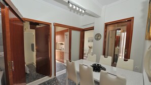A dining area with a table and chairs, a clock on the wall, and wooden doors leading to other rooms. - Themis 40 steps from beach - Dionisiou Halkidiki (Paralia Dionisiou)