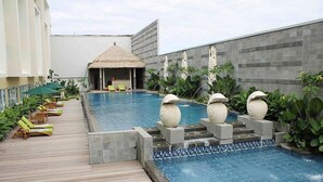 A pool area with lounge chairs, a thatched-roof structure, and decorative urns. - Grand Allison (Sentani)