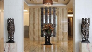 A lobby with marble flooring, a central floral arrangement on a glass table, and two wooden sculptures on pedestals. - Grand Allison (Sentani)