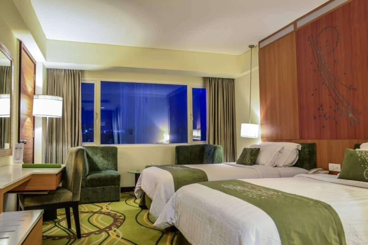 A hotel room with two beds, a desk, a chair, and a large window with curtains.