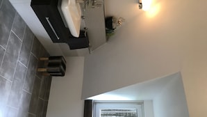 Een moderne badkamer met een witte wastafel, donkere tegels en een klein plantje.