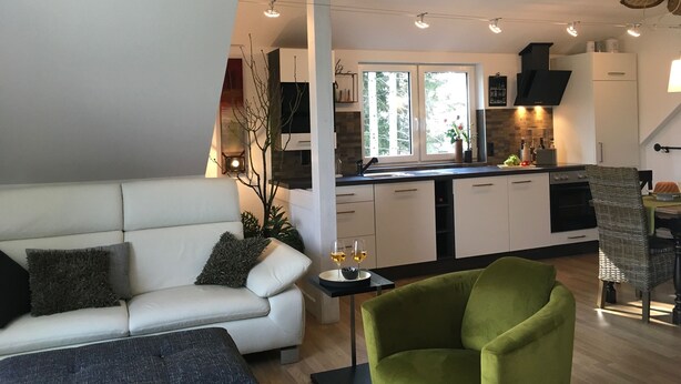 Een moderne woonkamer met een bank, een groene fauteuil en een eethoek met een tafel en stoelen.