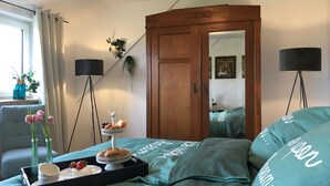 Een slaapkamer met een bed, een houten garderobe, een spiegel, een vloerlamp en een raam met gordijnen.